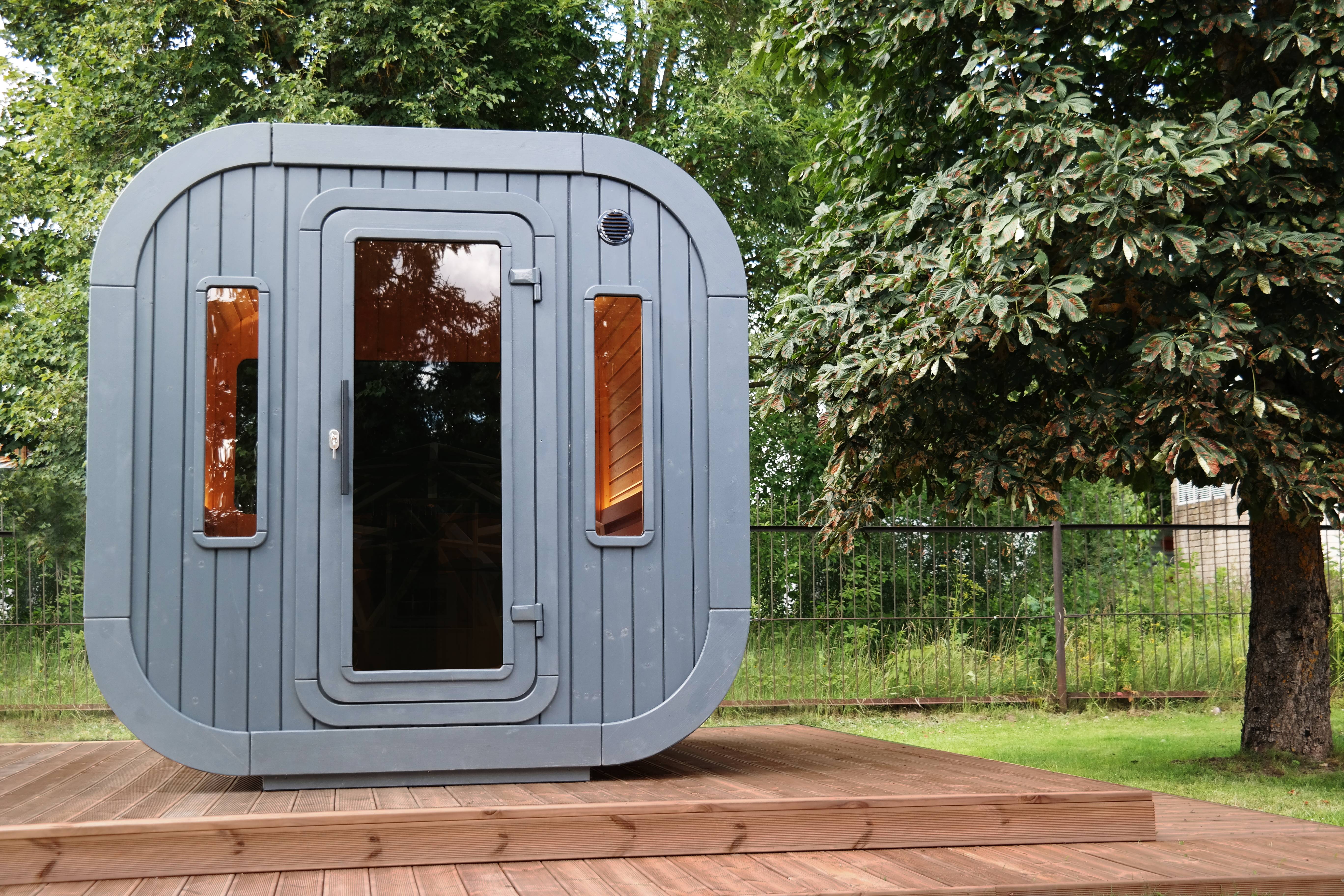 A black wood stained Luna sauna on a wooden terrace with trees in the background.