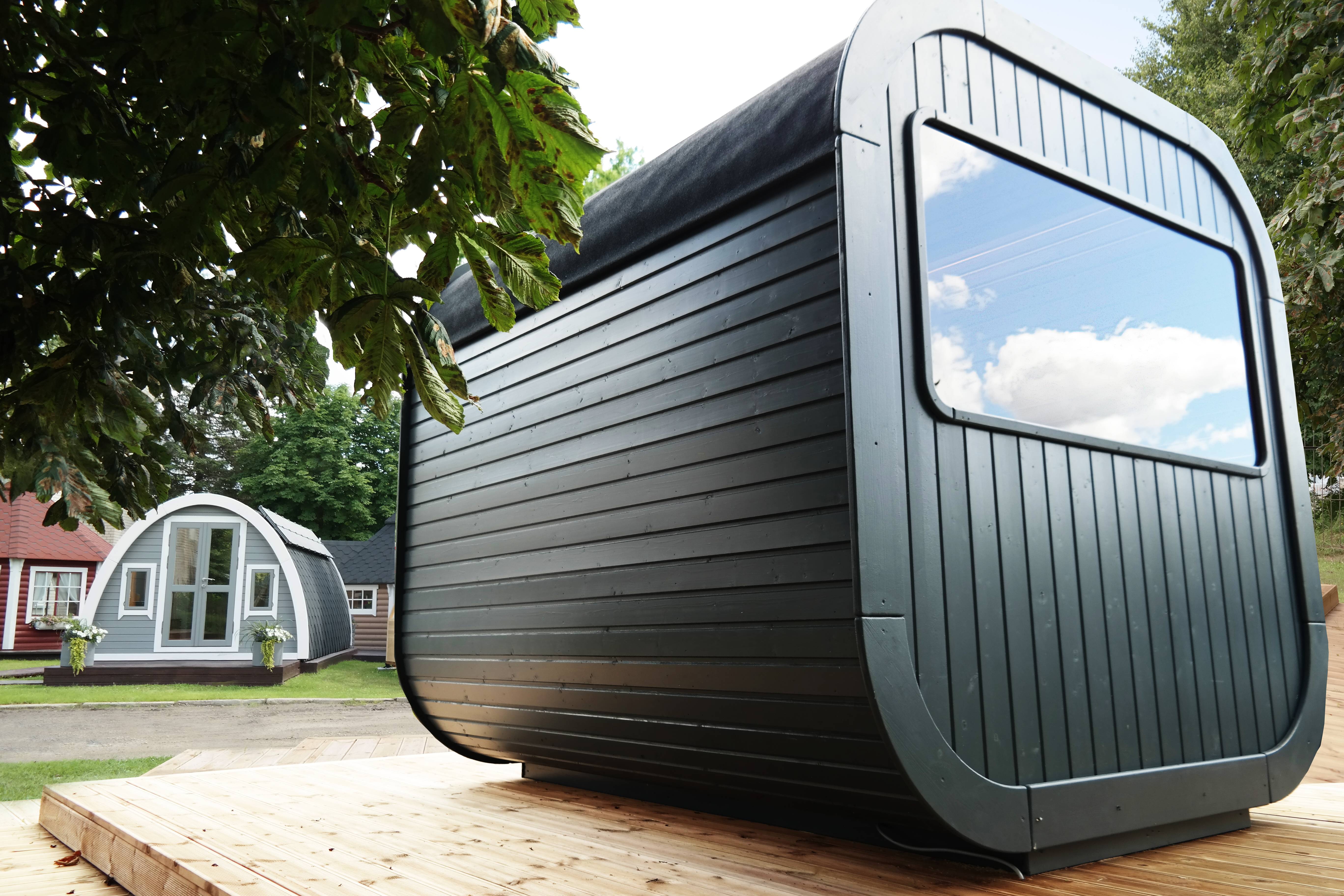 A rear angle view of the black finished Luna Sauna with a large glass window at the back on a wooden terrace.