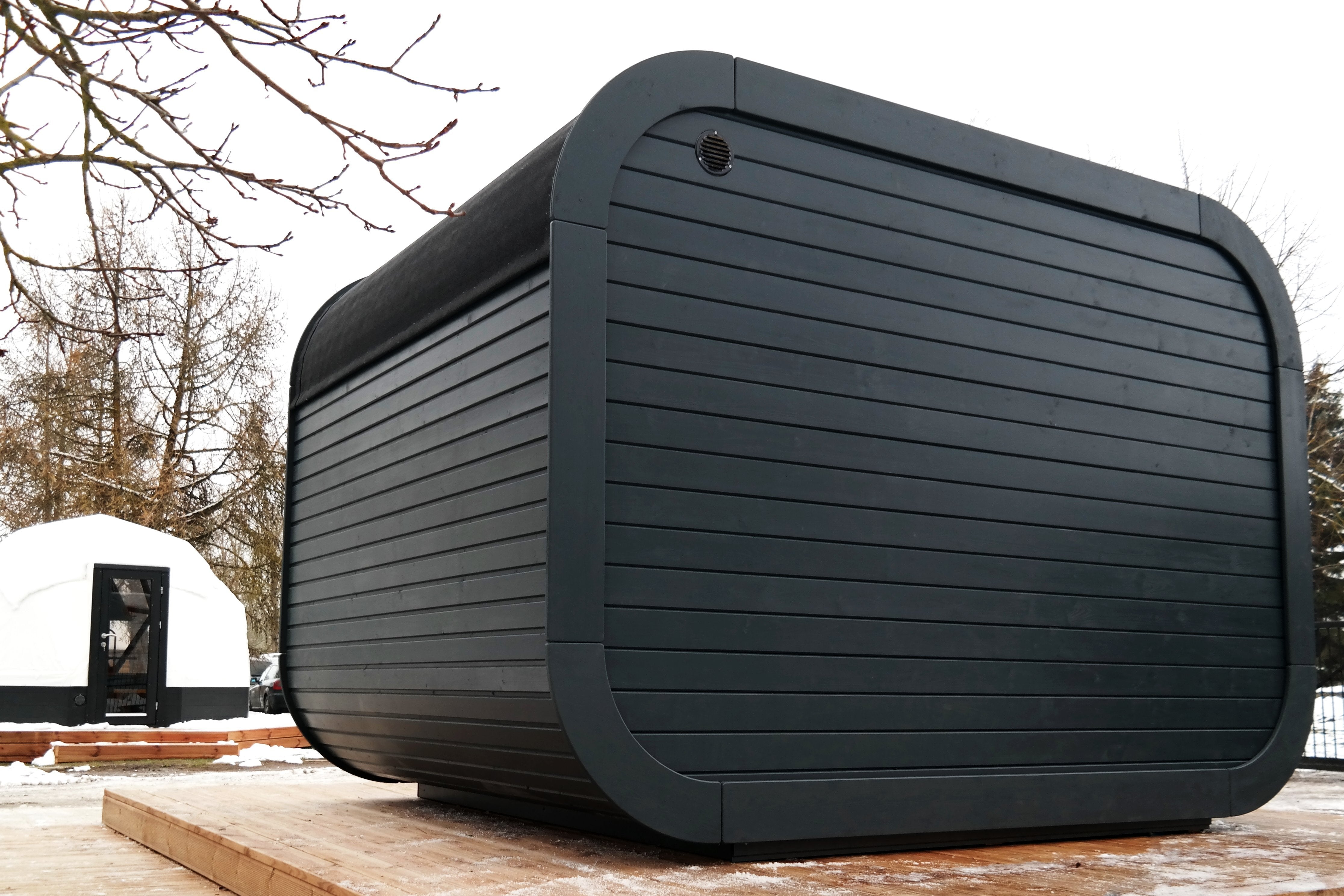 An image showing the back of the black Sauna with ventilation top left with the structure atop a wooden terrace. 