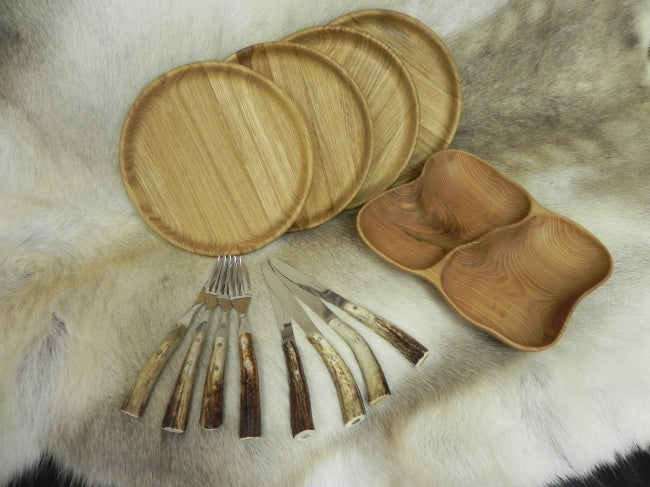 A top down image of 4 plates 4 sets of knives and forks and a double bowl dish set atop a reindeer hide these are accessories for the BBQ Hut's & Grills