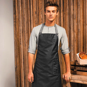 A man modelling the wax look denim apron with a wooden fence in the background