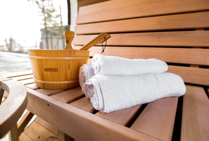 A Harvia bucket and paddle sat on top of a bench in a sauna with some towels beside it.