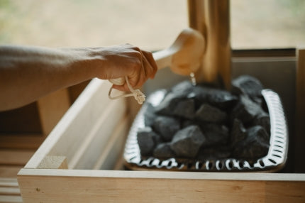 A wooden paddle being used by someone to put water onto the coals of a wood fired sauna heater.